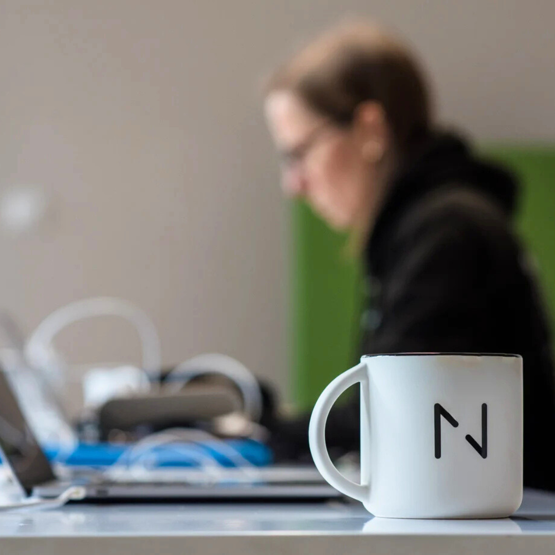 Woman working on a laptop with a mug with Netguru logo in the foreground