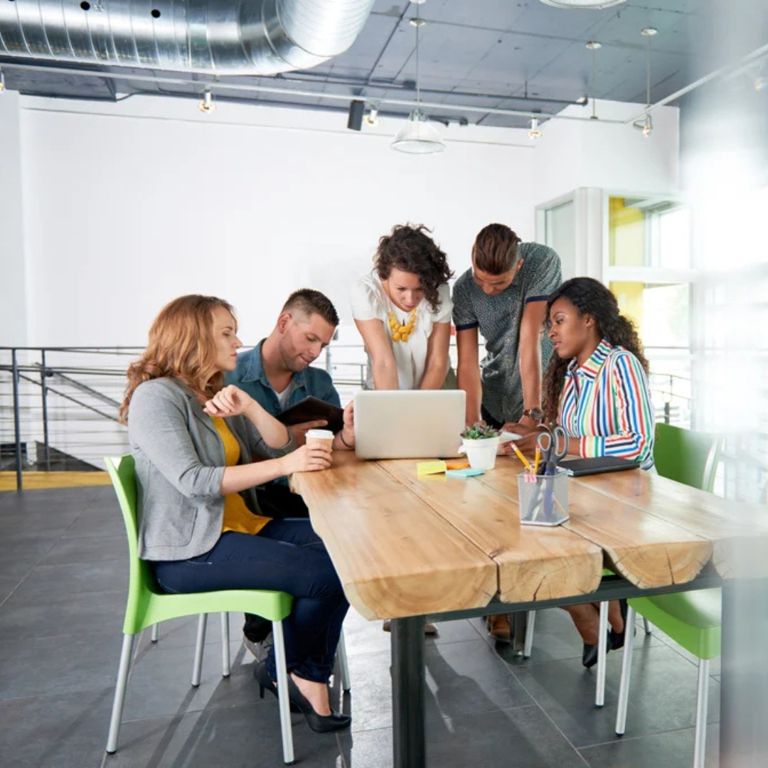 A group of working professionals gathered around a laptop placed on a table