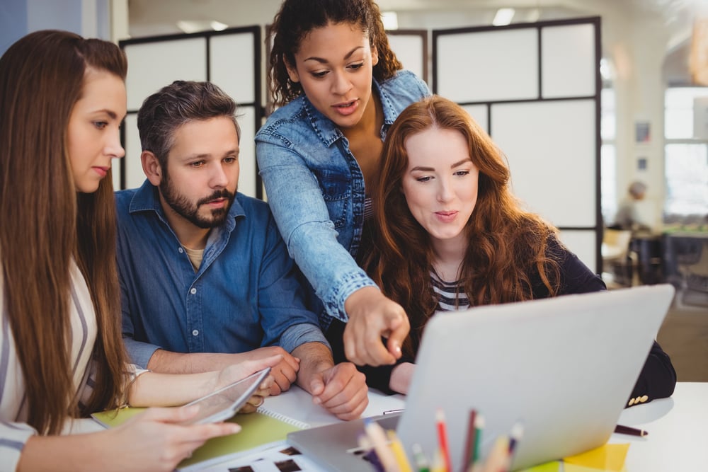 Businesswoman pointing at laptop with coworkers at desk in creative office-2