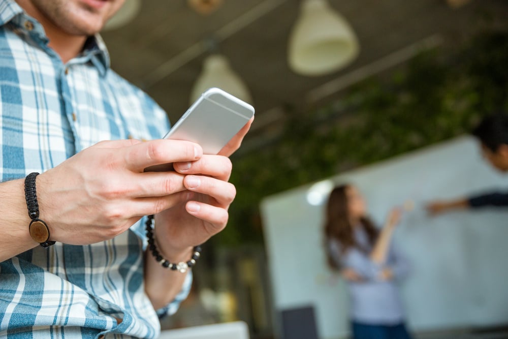 Closeup of hands of young man in checkered shirt using mobile phone while his partners arguing-4