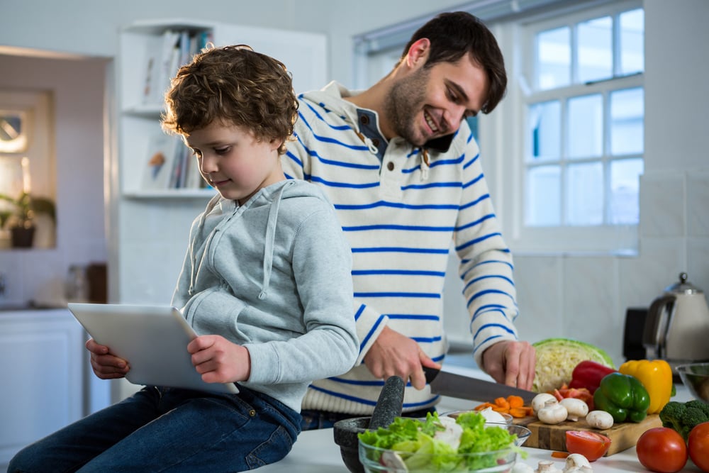 Father talking on mobile phone while chopping vegetables and son using digital tablet in the kitchen-1