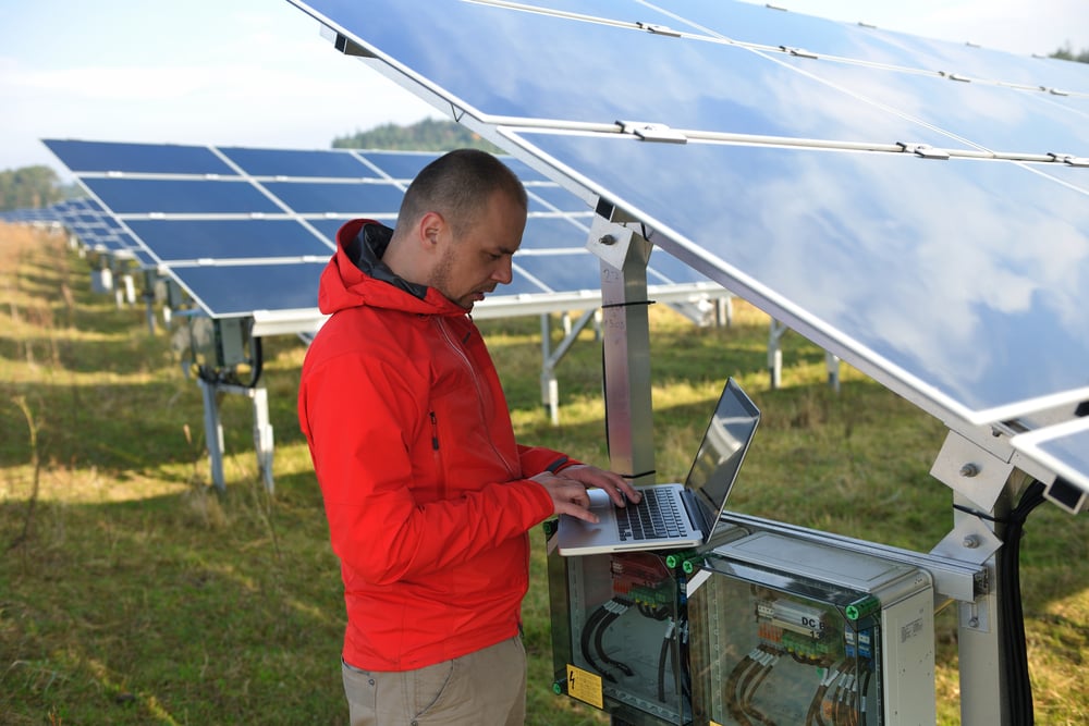 business man engineer using laptop at solar panels plant eco energy field in background