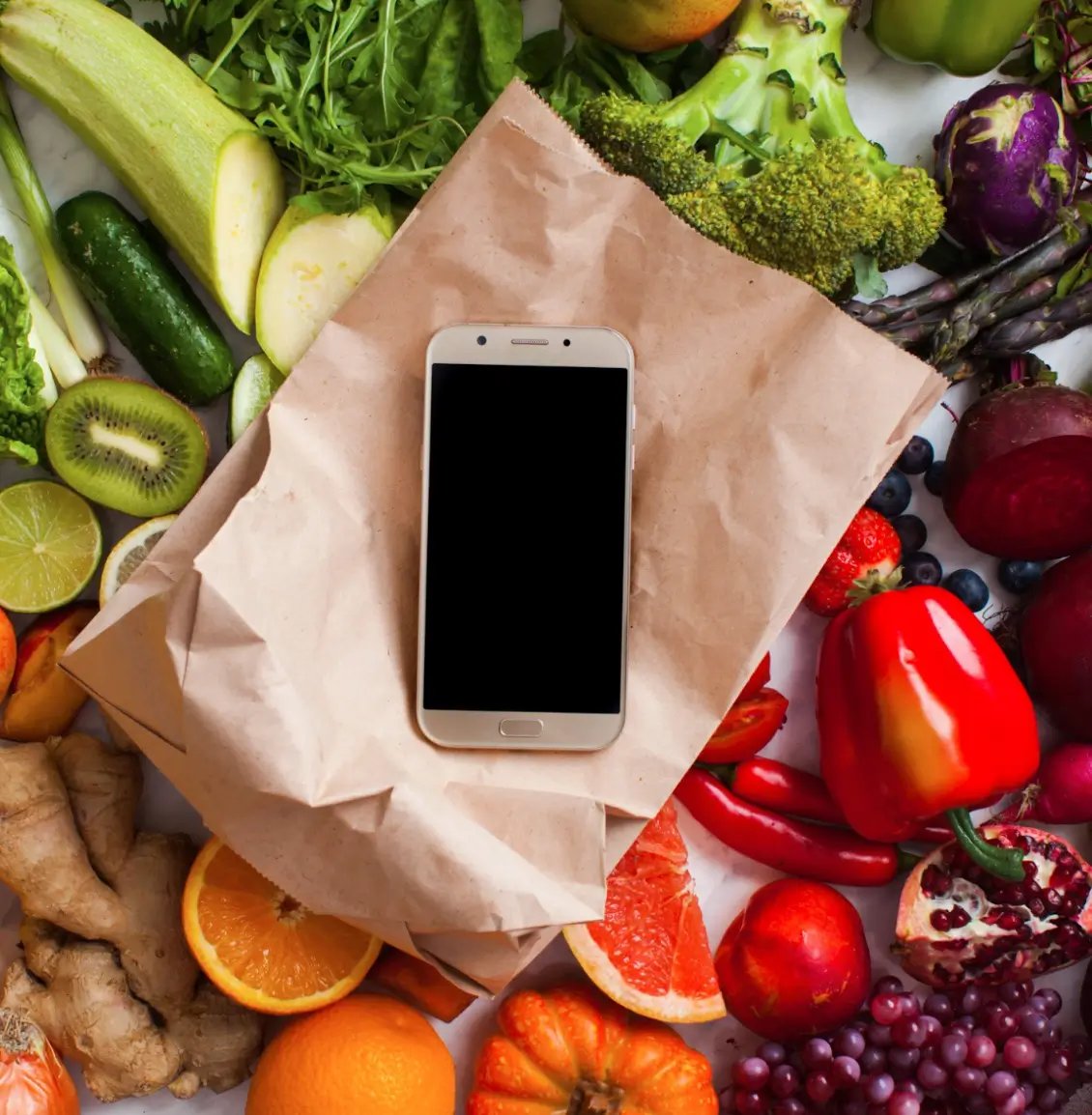 a phone laying on a table full of fruits and veggies