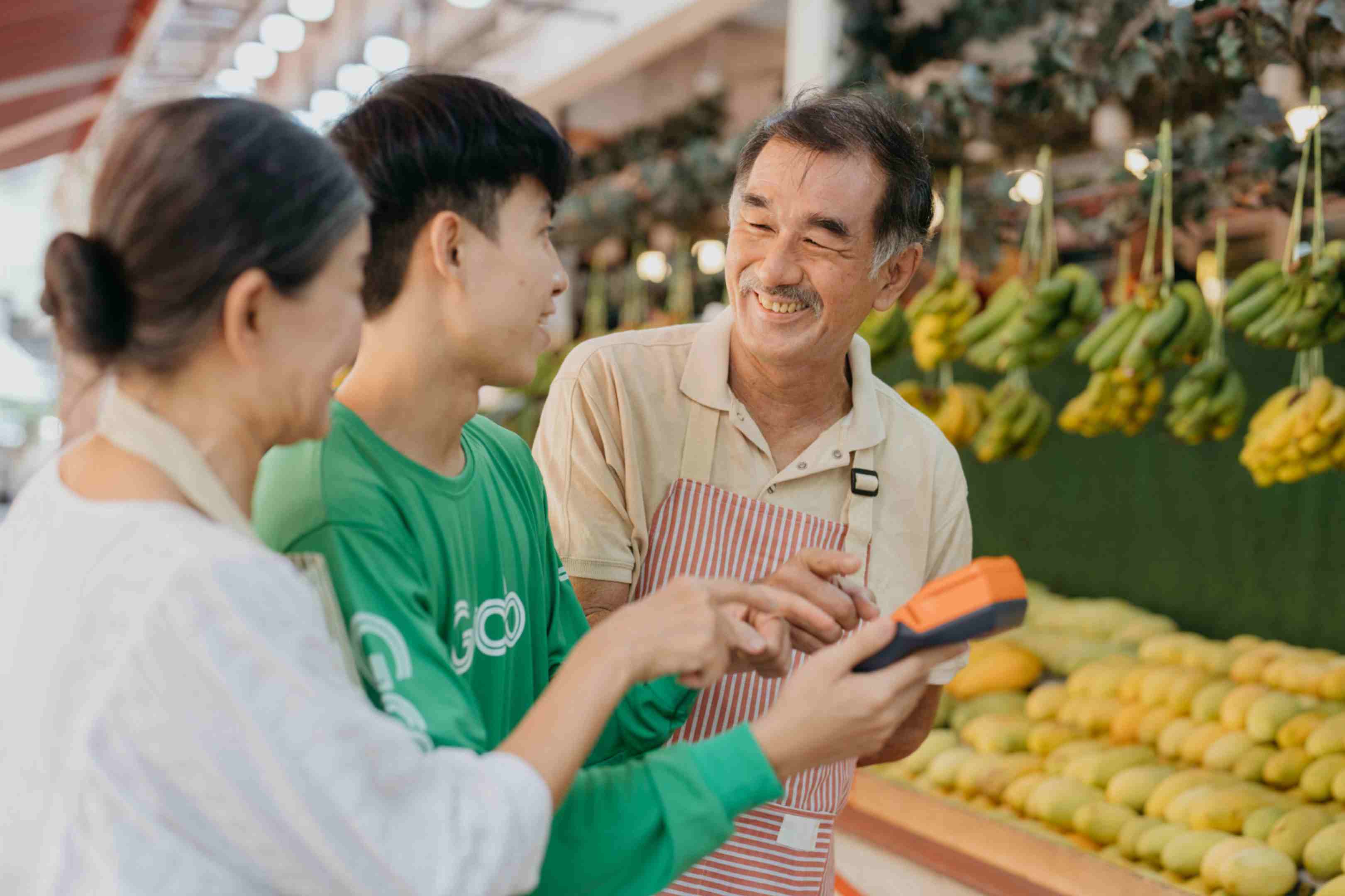 A grocery shop staff member with a terminal smiling at a pair of customers