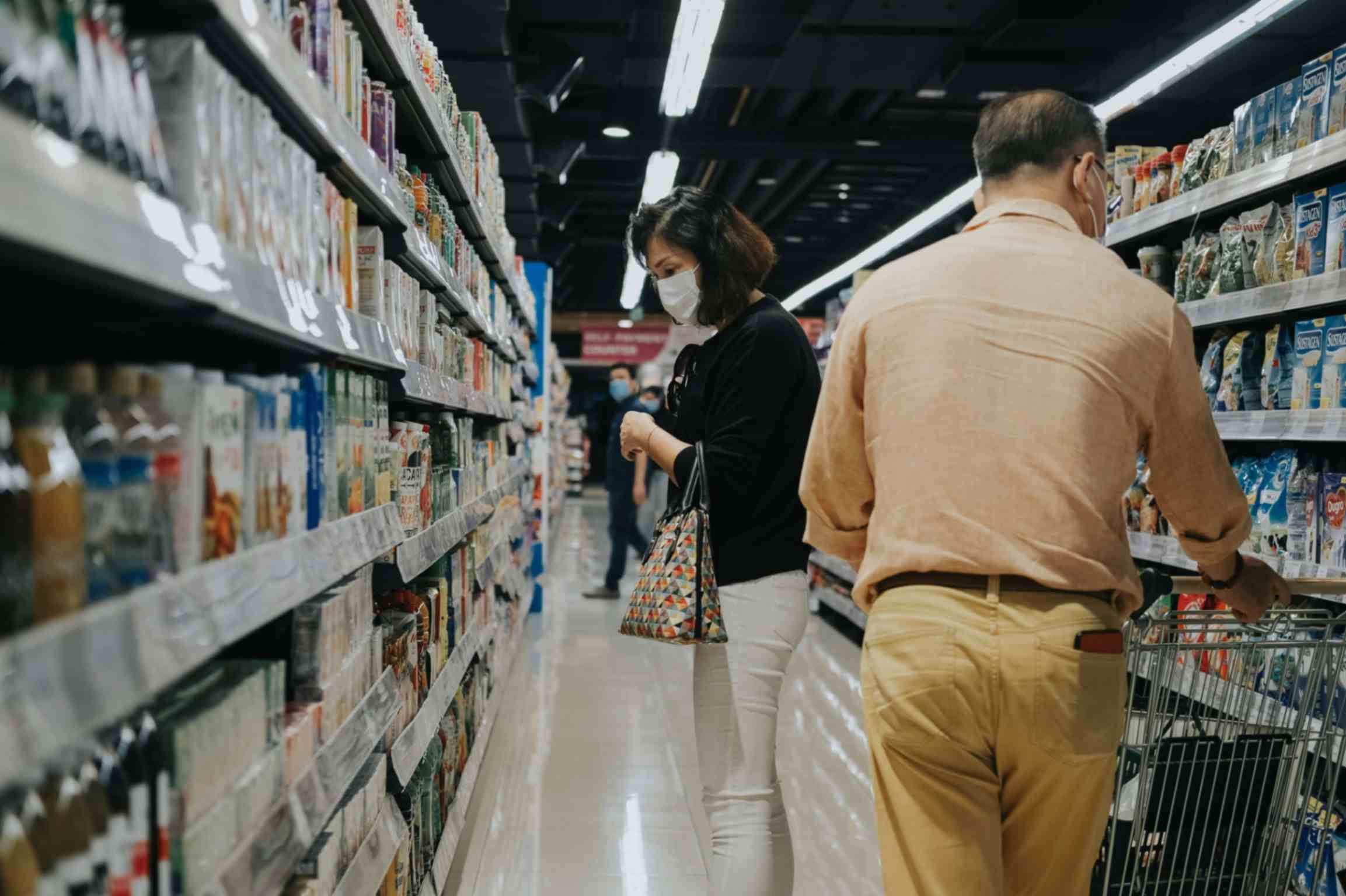 Woman (side-view) and man (back-view) wearing face masks in a grocery store aisle