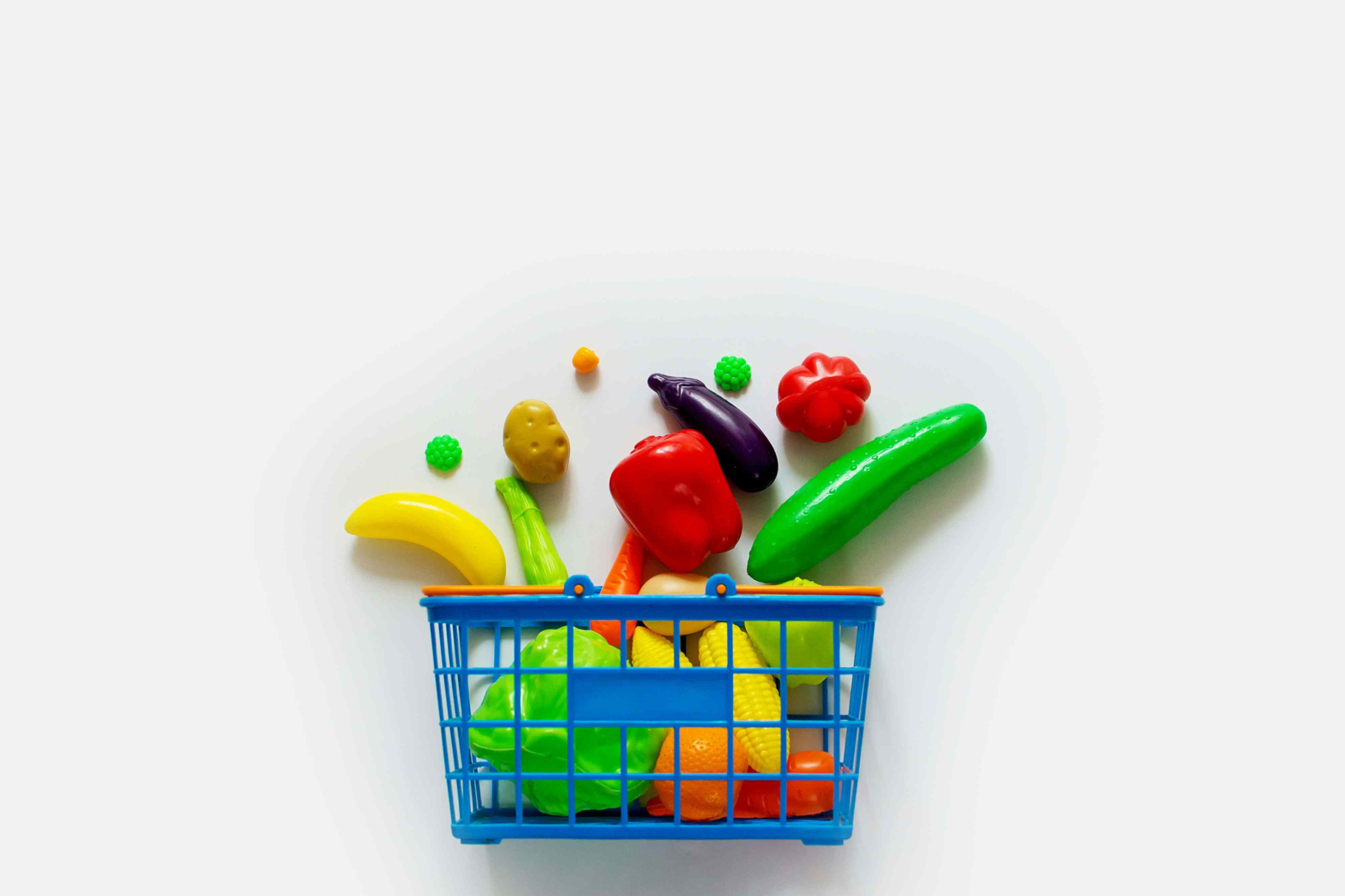 a blue shopping basket with food items inside and spilling out onto white background
